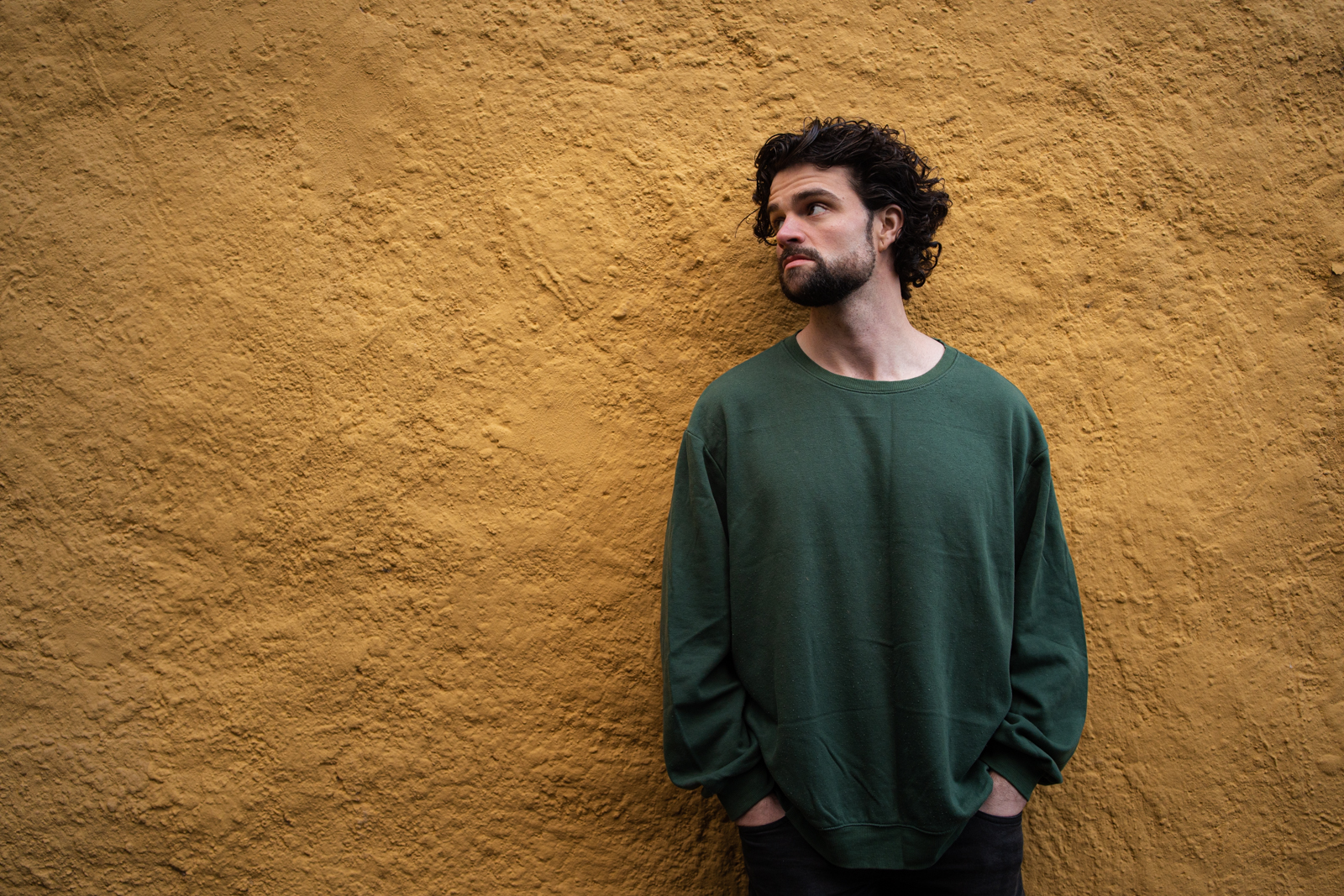 Luke Nederveen in a green sweater against a mustard wall